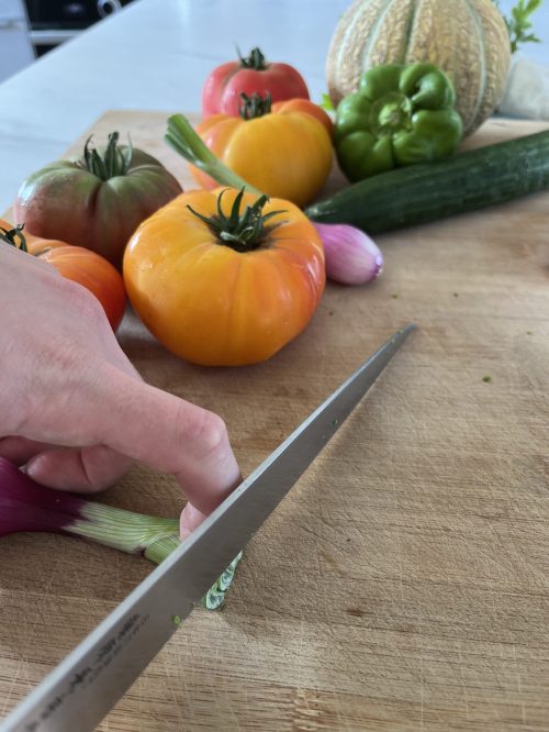 légumes sur plan de travail avec couteau qui les coupe, main visible